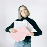 Confident woman holding tax documents in casual attire, ready for filing.